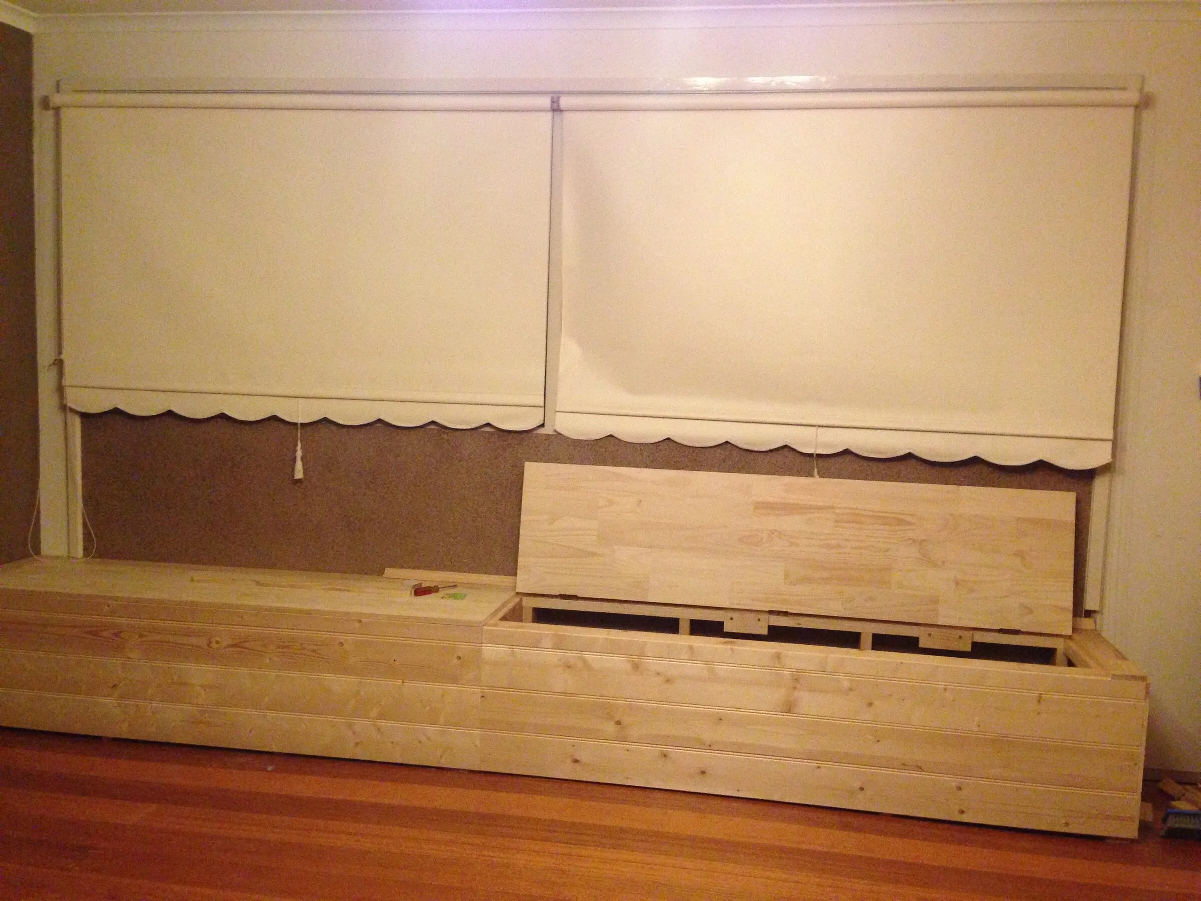 A pine window seat with storage under, built in beneath the blinds and waiting for its finish.