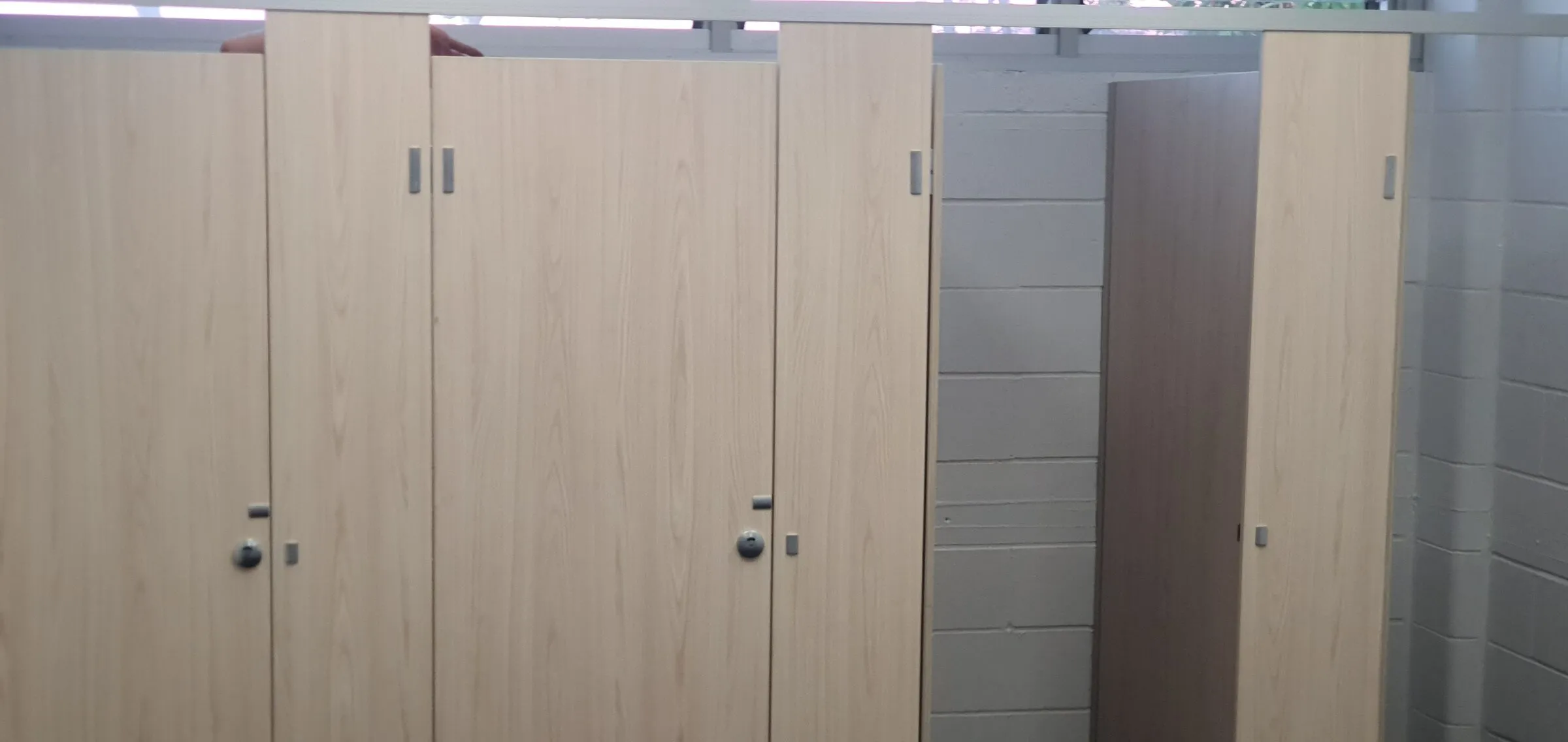 Timber-look cubicle doors and pilasters refitted in a public change room, closed and hanging square.