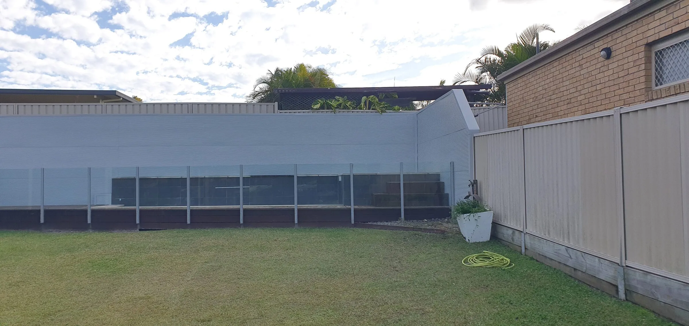 New colourbond panels added above the existing glazed screen along a rear boundary, seen from the lawn.