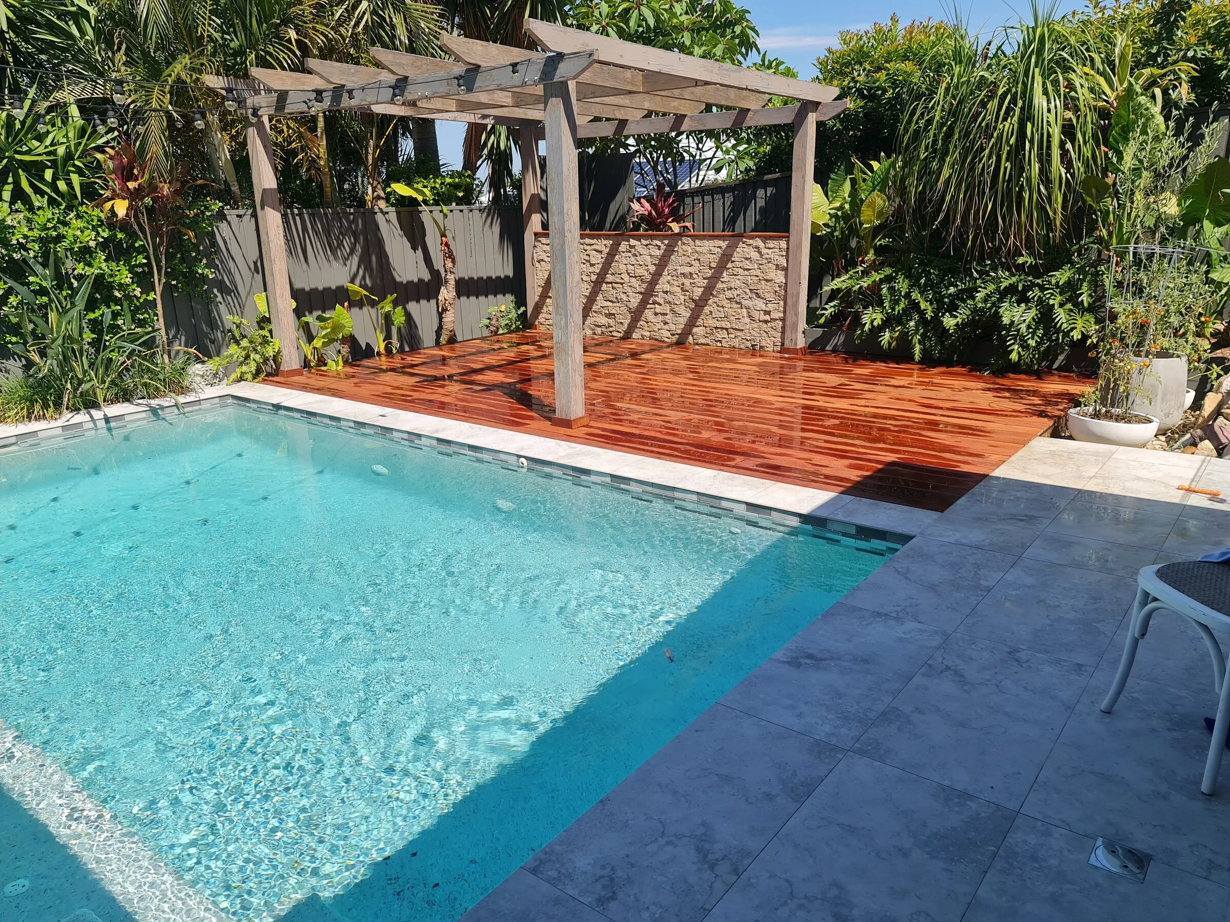 A hardwood poolside deck after board repairs and re-oiling, finished up to the stone coping.