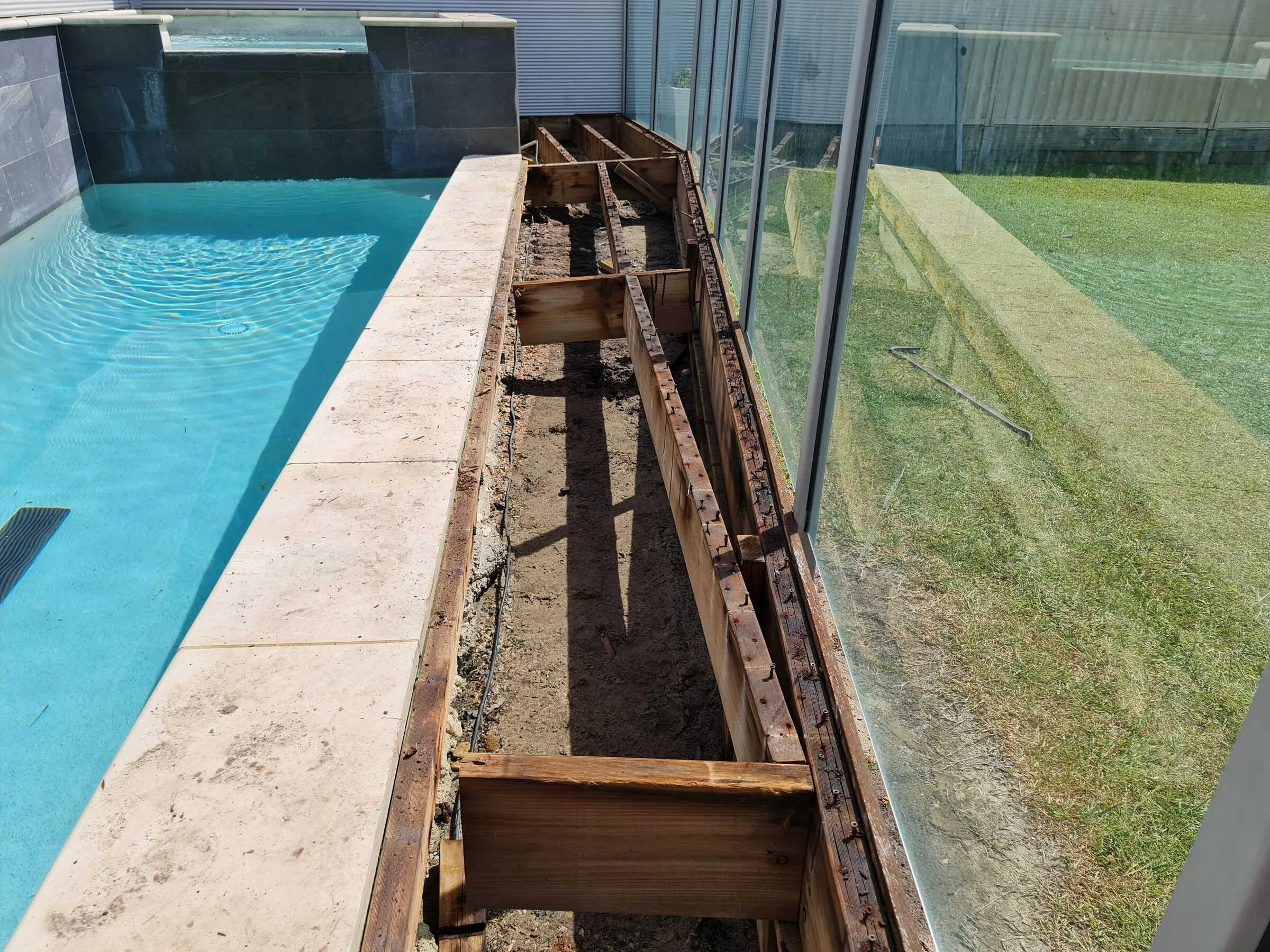 Decking lifted beside a lap pool, showing the rotted bearers and joists underneath.