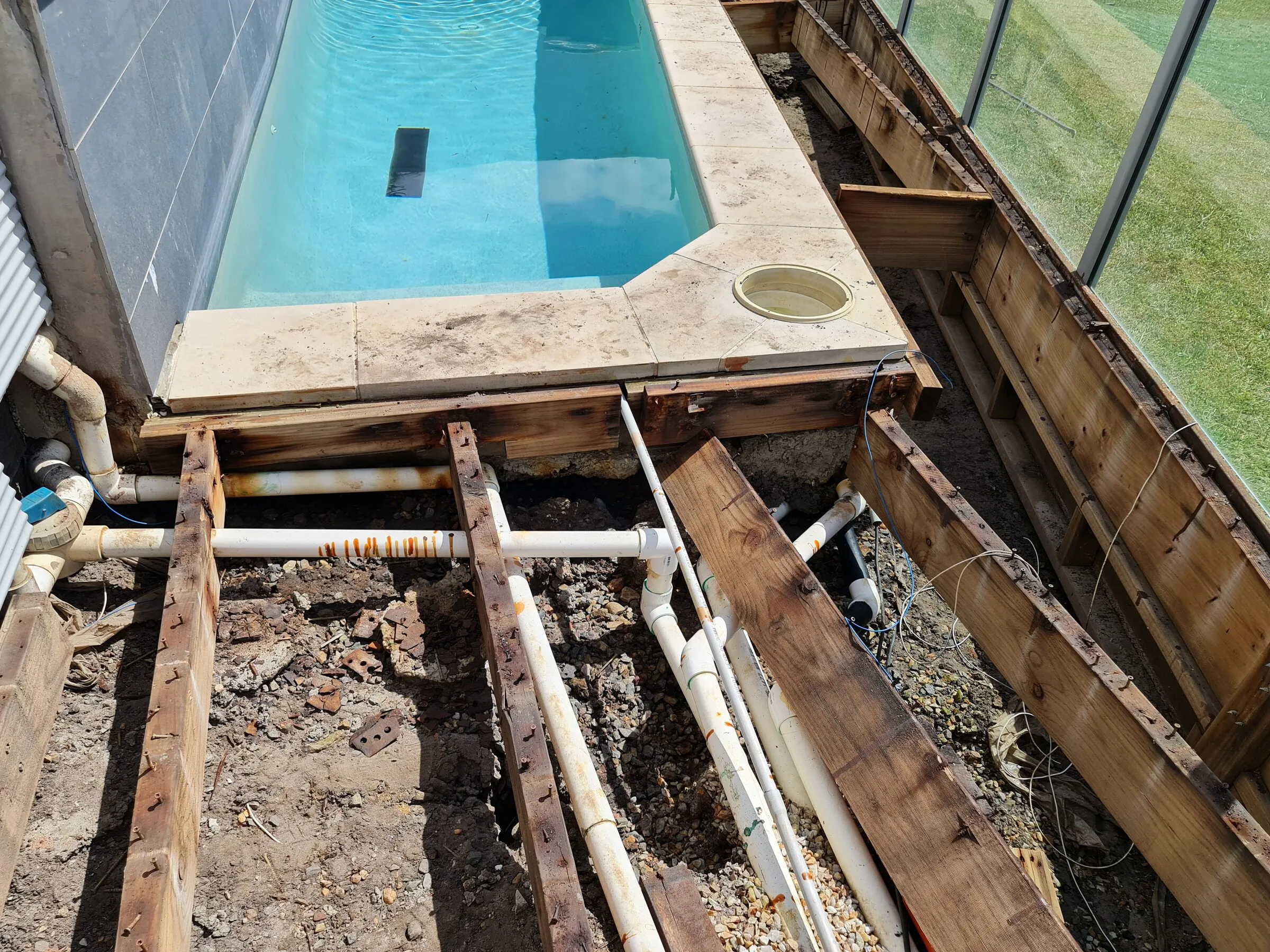 The stripped-out pool surround with rotted bearers, rusted fixings and the pipework exposed.
