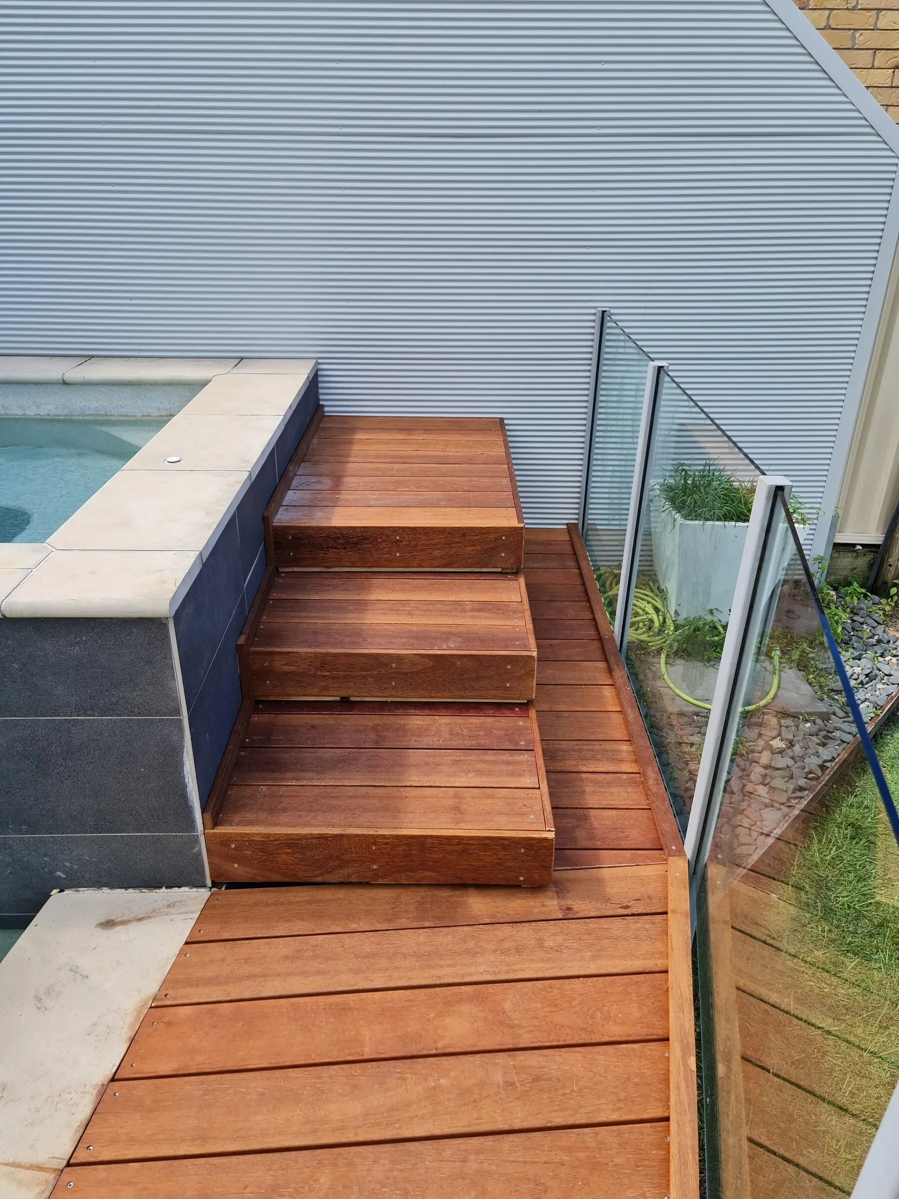 Hardwood steps and deck alongside the pool after repair, looking back along the glazed screen.