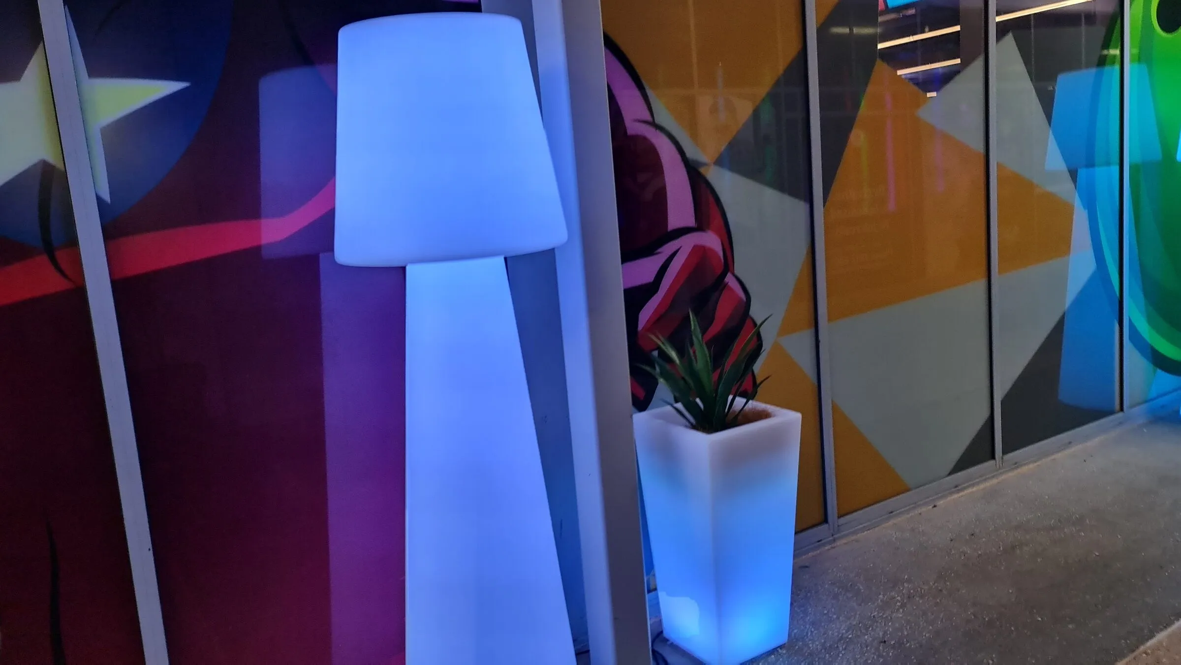 A close view of one illuminated lamp and planter standing against the walkway glazing.