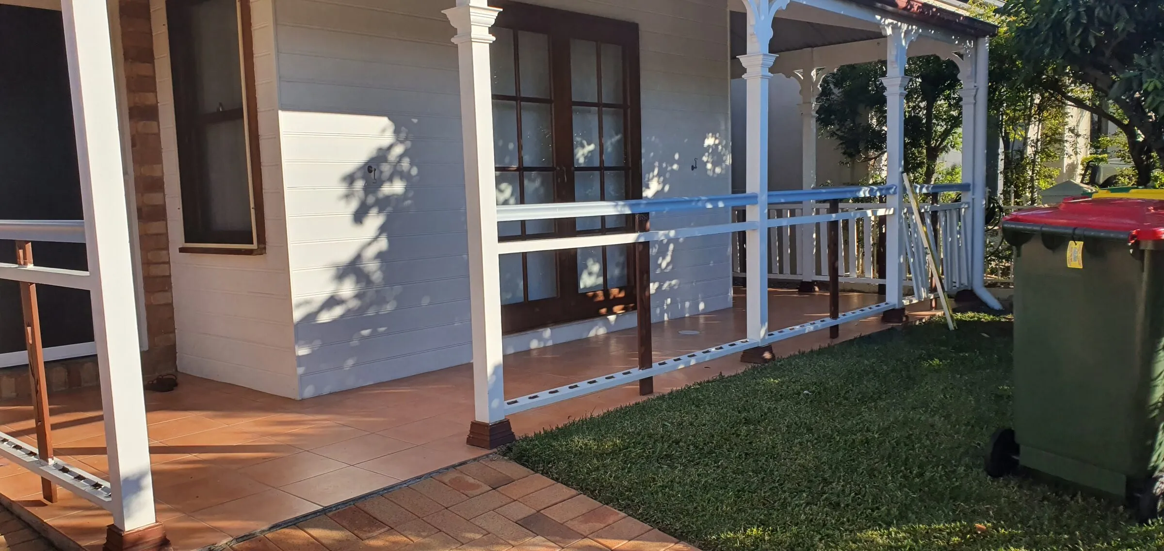 The open front of a timber cottage with the old balustrade stripped out and temporary rails strapped across the posts.