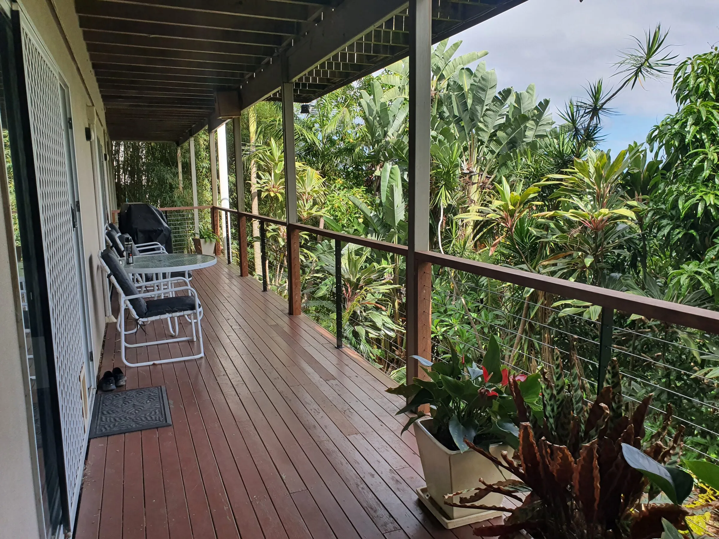 A hardwood deck running the length of the house, wire balustrade and timber top rail, table and chairs out.