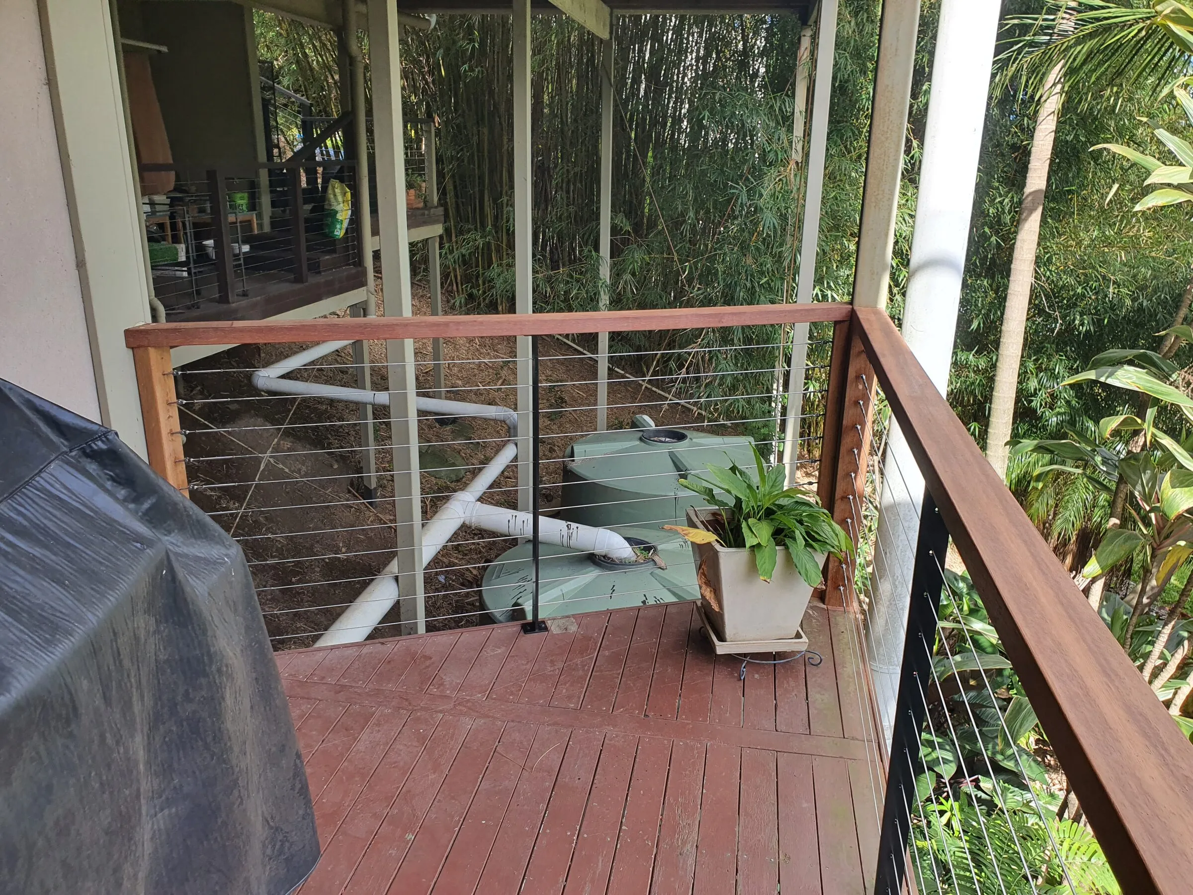 The corner of the same deck, wire balustrade and hardwood top rail against the bamboo behind.