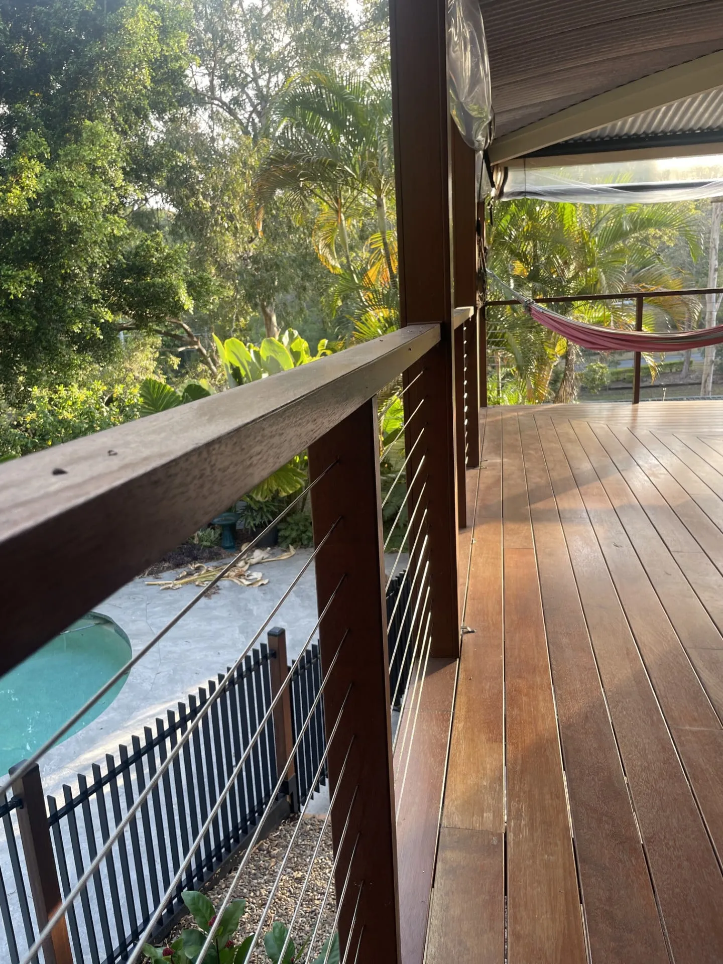 Timber deck with stainless steel wire balustrade and timber top rail, overlooking a pool and garden.
